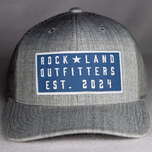 Rock Land Outfitters Blue Logo Patch On A Heather Gray Trucker Hat