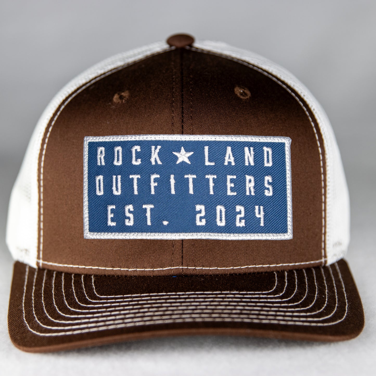 Rock Land Outfitters Blue Logo Patch On A Brown And White Hat